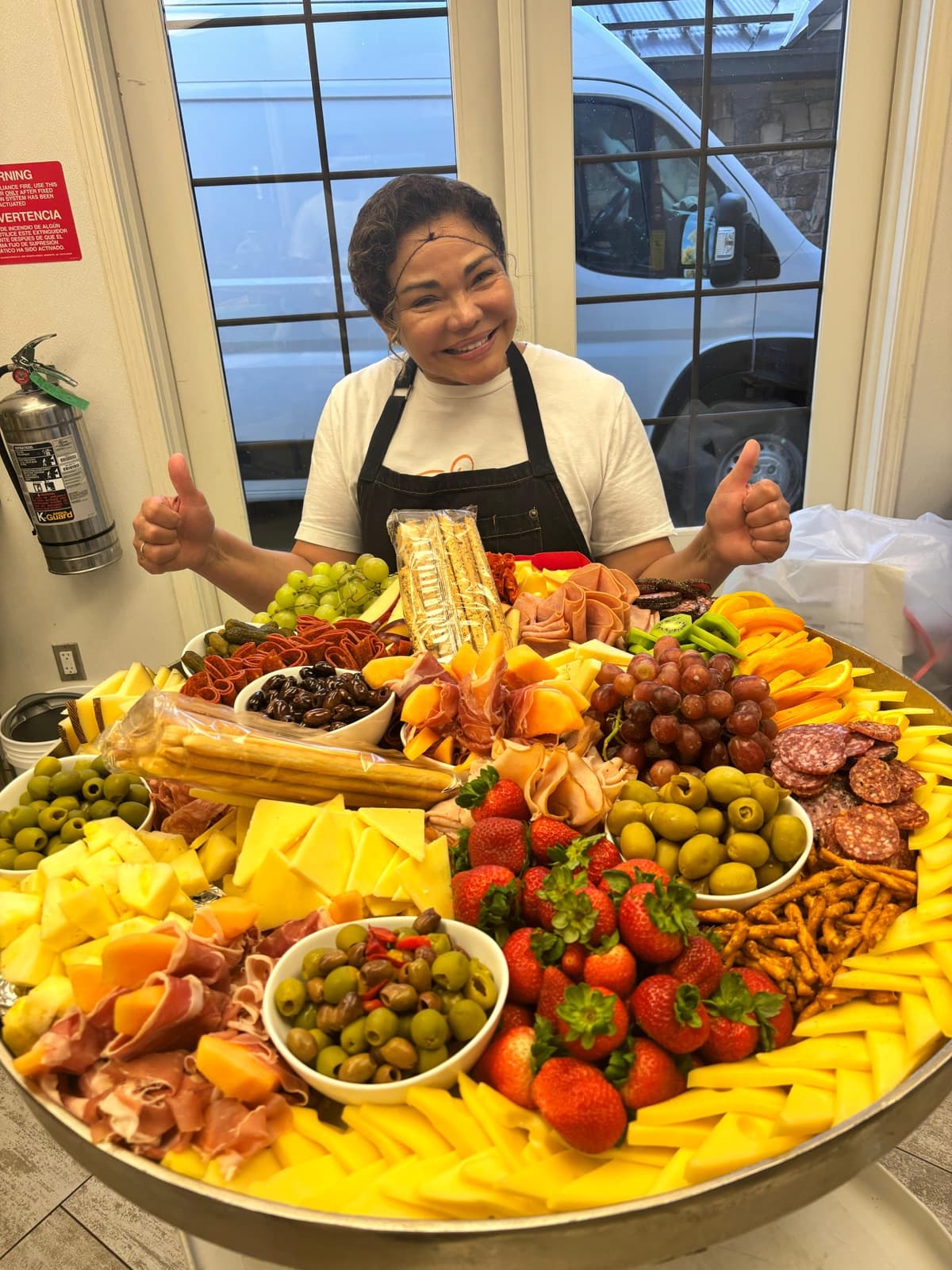 Patty smiling behind an enormous charcuterie board with cheeses, cured meats, olives, and fresh fruit