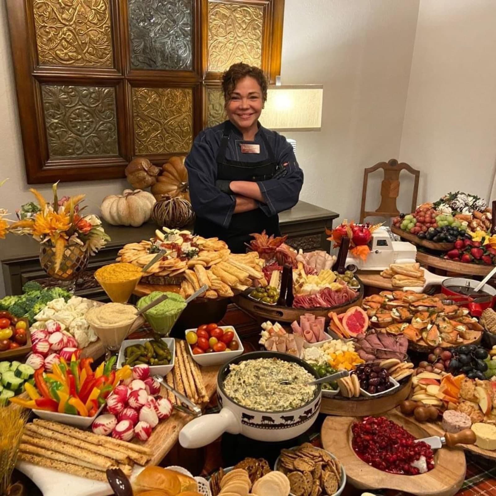 Patty in her chef's coat behind an abundant grazing table of charcuterie, fruit, and fresh vegetables