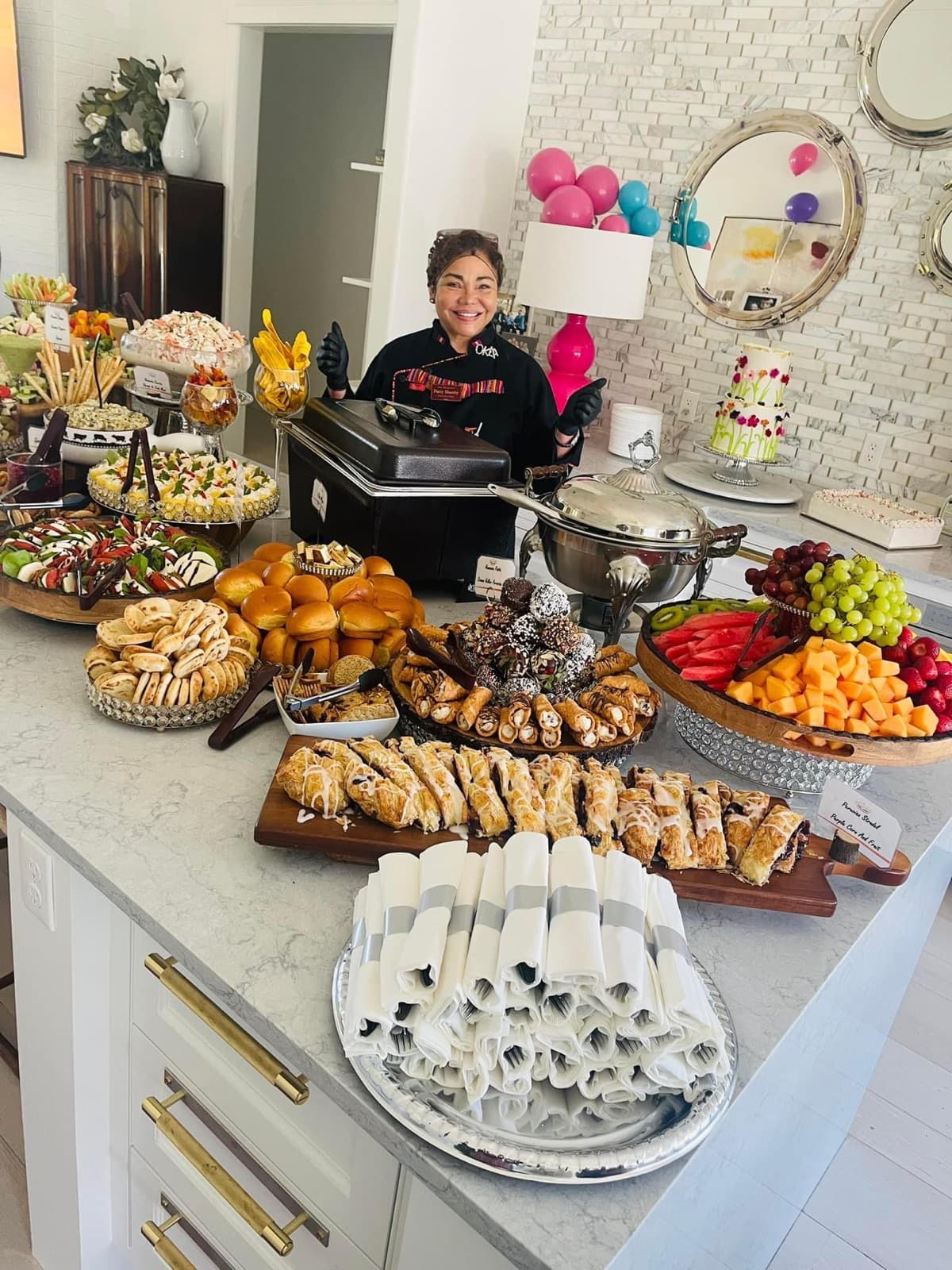 Patty beside an abundant party catering spread with pastries, fruit, and charcuterie